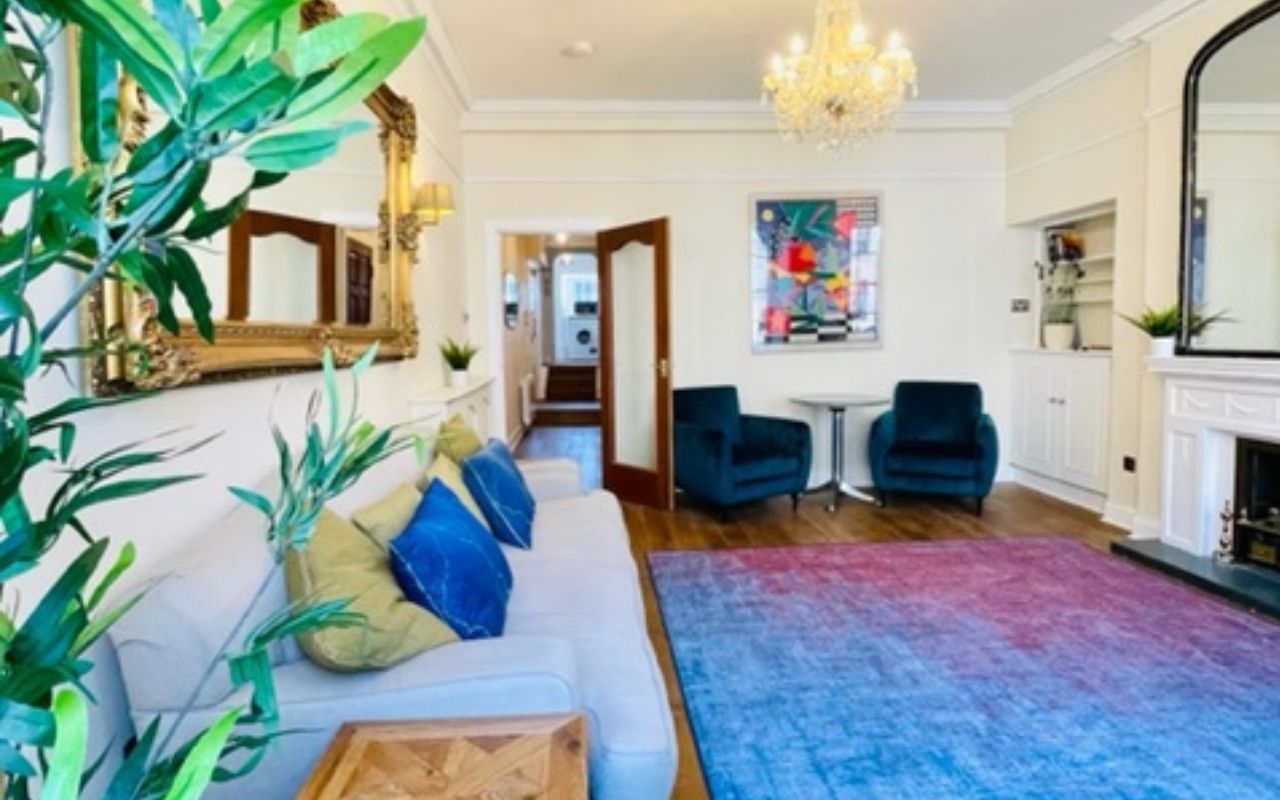 Royal Mile Apartment 1 Colourful living room with chandelier, blue sofa and patterned rug at The City Apartments Edinburgh